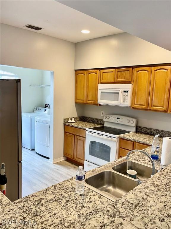 kitchen featuring sink, washer and dryer, white appliances, and light wood-type flooring