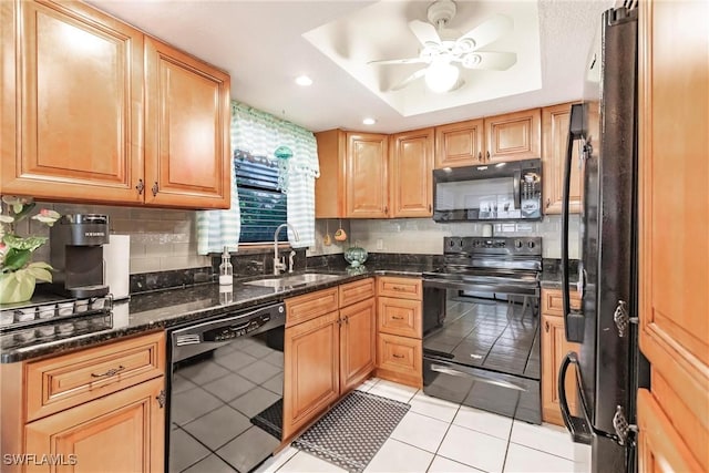 kitchen featuring a raised ceiling, ceiling fan, sink, black appliances, and dark stone countertops