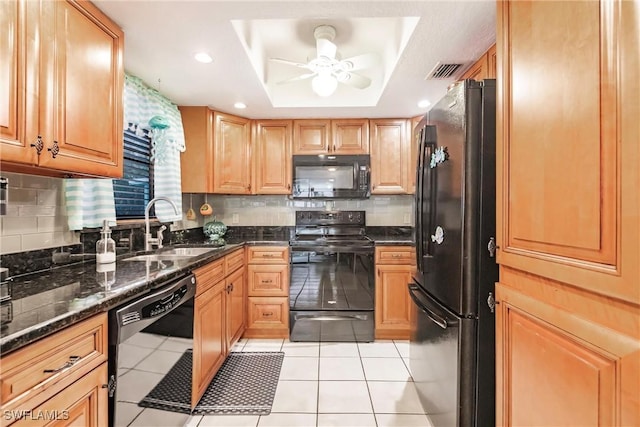 kitchen featuring dark stone counters, a raised ceiling, ceiling fan, sink, and black appliances