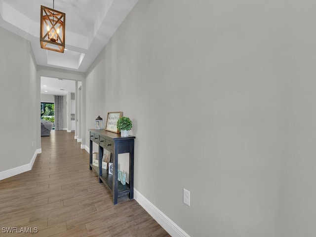 hall featuring an inviting chandelier, a raised ceiling, baseboards, and wood finished floors