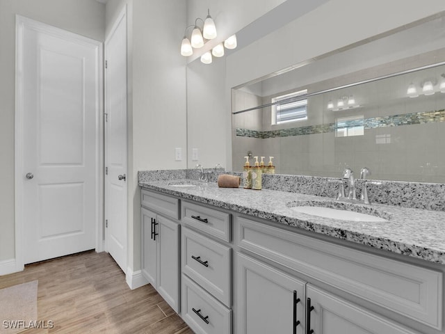 bathroom with wood finished floors, double vanity, a sink, and a walk in shower