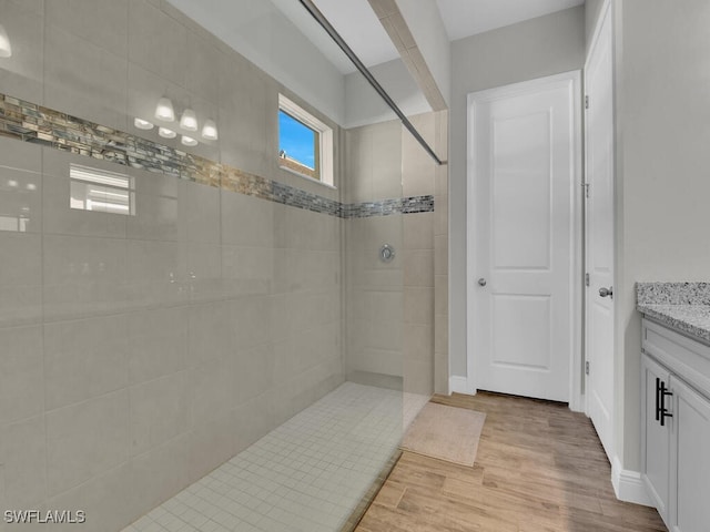 bathroom featuring a tile shower, wood finished floors, and vanity