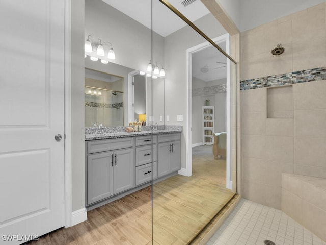 bathroom with double vanity, a sink, wood finished floors, baseboards, and walk in shower