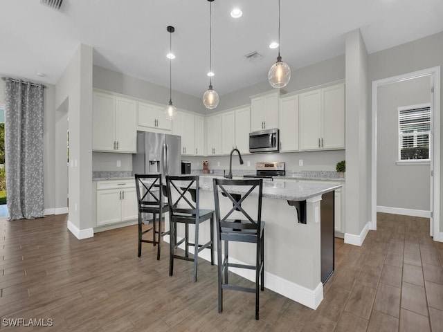 kitchen with light stone counters, a center island with sink, visible vents, appliances with stainless steel finishes, and white cabinetry