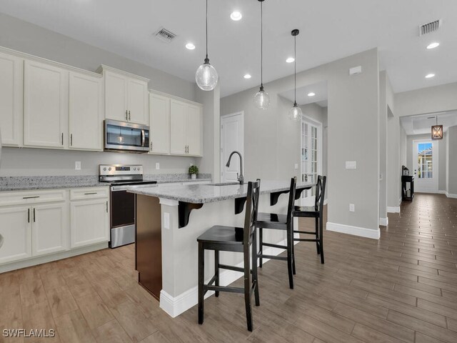 kitchen with appliances with stainless steel finishes, white cabinetry, a sink, and an island with sink