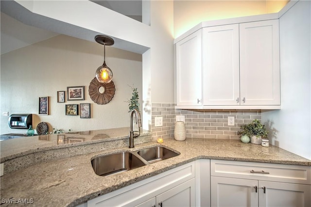 kitchen featuring white cabinets, pendant lighting, light stone countertops, and sink