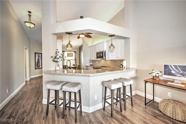 kitchen with hanging light fixtures, high vaulted ceiling, kitchen peninsula, decorative backsplash, and a breakfast bar