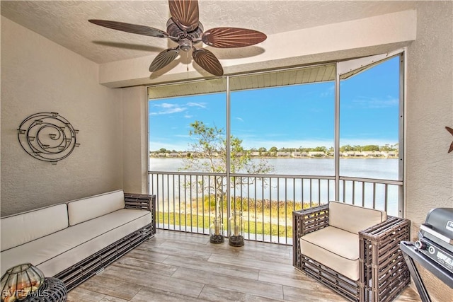 sunroom with ceiling fan and a water view