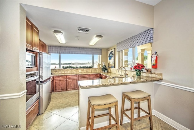 kitchen with sink, light stone counters, kitchen peninsula, oven, and a kitchen bar