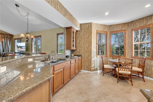 kitchen featuring light stone countertops, sink, a notable chandelier, pendant lighting, and wooden walls