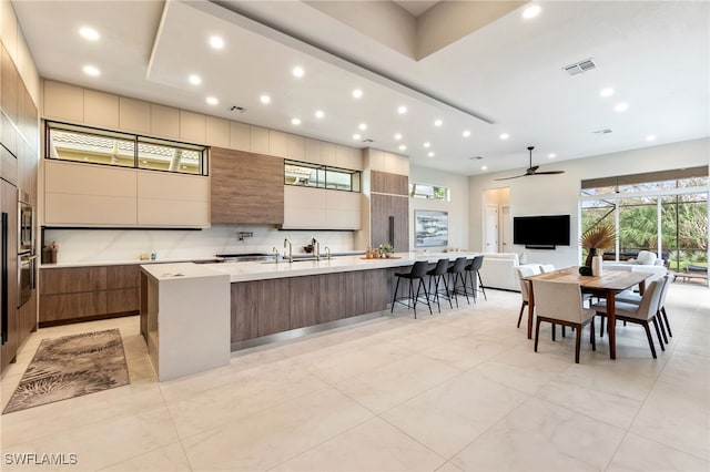 kitchen featuring a kitchen bar, backsplash, a large island with sink, and stainless steel oven