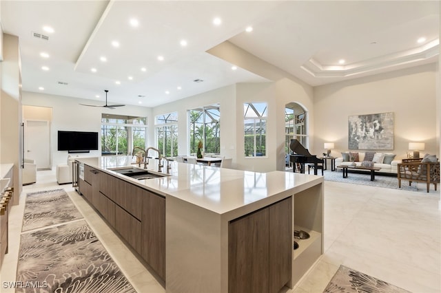 kitchen with sink, a large island, ceiling fan, a tray ceiling, and dark brown cabinets