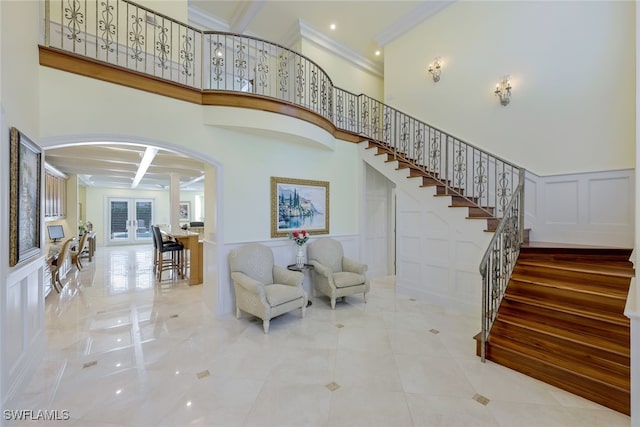 stairs featuring coffered ceiling, ornamental molding, a high ceiling, french doors, and a decorative wall