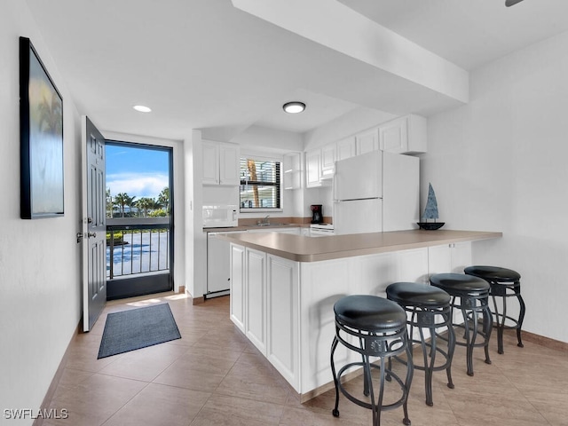 kitchen with white appliances, kitchen peninsula, light tile patterned floors, a kitchen bar, and white cabinetry