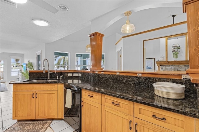 kitchen featuring sink, light tile patterned floors, decorative light fixtures, dark stone countertops, and dishwasher