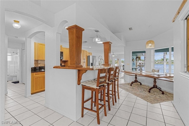 kitchen with backsplash, stainless steel refrigerator with ice dispenser, light tile patterned floors, ornate columns, and light brown cabinetry