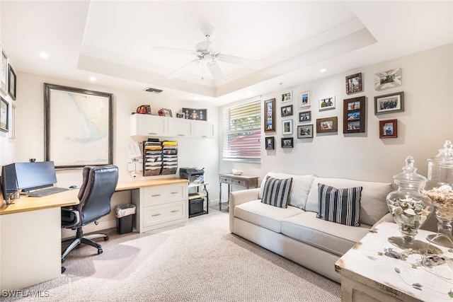 office space featuring built in desk, a tray ceiling, ceiling fan, and light colored carpet