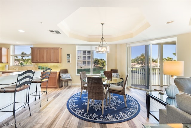 dining area featuring a raised ceiling, sink, light hardwood / wood-style flooring, and an inviting chandelier