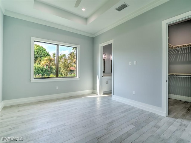 unfurnished bedroom with connected bathroom, light hardwood / wood-style flooring, a walk in closet, a closet, and ornamental molding