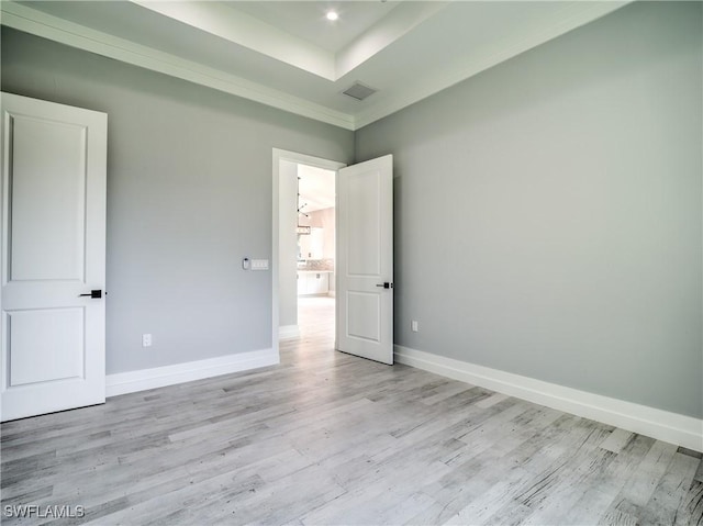 unfurnished room featuring a tray ceiling, crown molding, and light hardwood / wood-style flooring