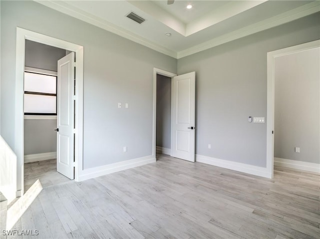 unfurnished bedroom with a raised ceiling, ornamental molding, and light wood-type flooring