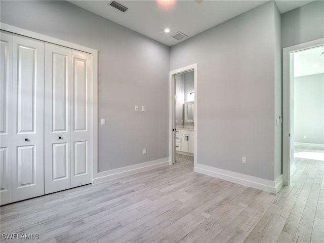 unfurnished bedroom featuring ensuite bath, a closet, and light hardwood / wood-style flooring