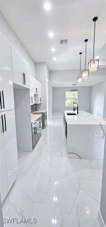 kitchen with light stone countertops, sink, hanging light fixtures, a center island with sink, and white cabinets