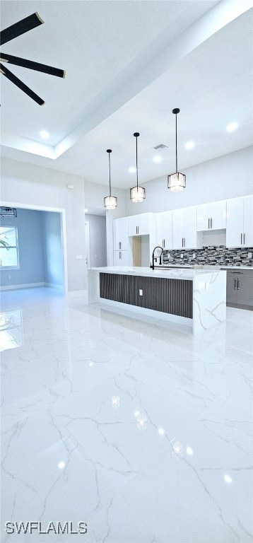 kitchen featuring pendant lighting, white cabinetry, ceiling fan, and an island with sink