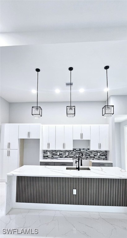 interior space featuring white cabinets, an island with sink, hanging light fixtures, and sink