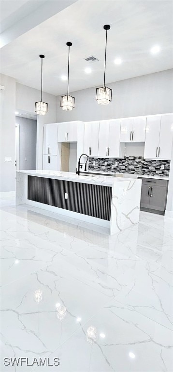 kitchen featuring pendant lighting, light stone counters, white cabinetry, and sink