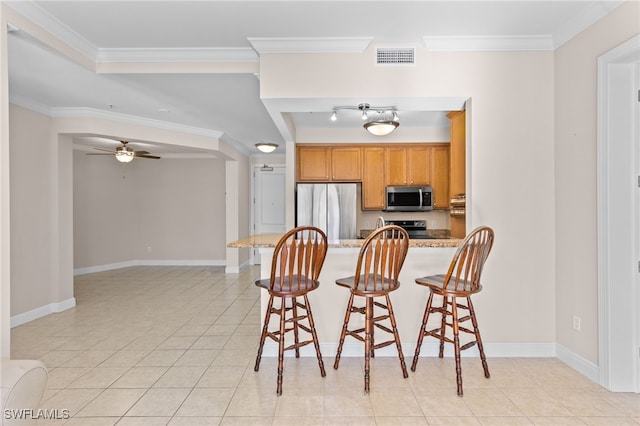 kitchen featuring light tile patterned floors, stainless steel appliances, light stone countertops, and a breakfast bar area