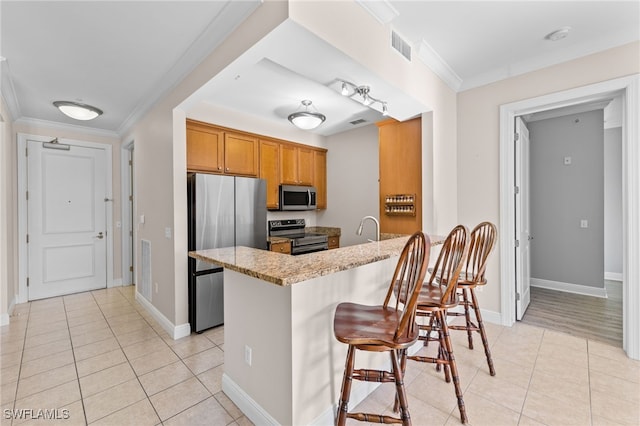 kitchen featuring a kitchen bar, light tile patterned floors, stainless steel appliances, light stone countertops, and ornamental molding