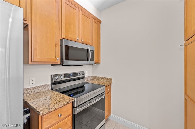 kitchen featuring appliances with stainless steel finishes, light tile patterned flooring, and light stone counters