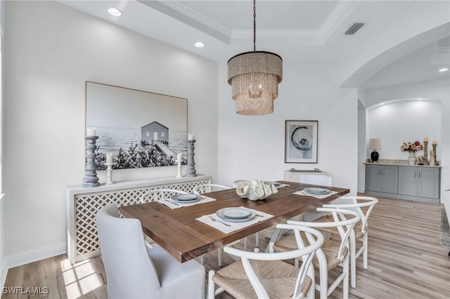 dining room featuring an inviting chandelier, a raised ceiling, crown molding, and light hardwood / wood-style flooring