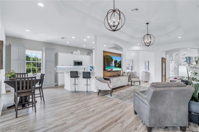 living room with an inviting chandelier, light hardwood / wood-style flooring, and a raised ceiling