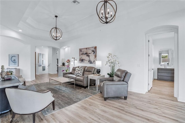 living room with a notable chandelier, light wood-type flooring, and a tray ceiling