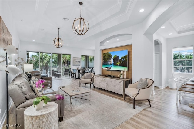 living room featuring a raised ceiling, crown molding, light hardwood / wood-style floors, and a notable chandelier