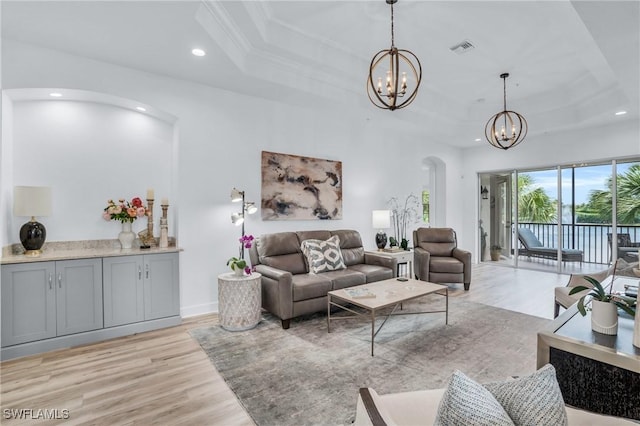 living room with a chandelier, light hardwood / wood-style floors, and a tray ceiling