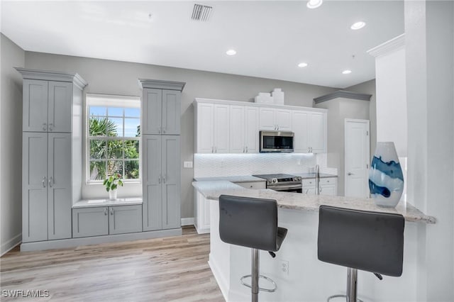 kitchen featuring light stone countertops, appliances with stainless steel finishes, light wood-type flooring, and backsplash