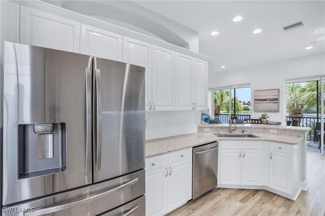 kitchen with white cabinets, light wood-type flooring, appliances with stainless steel finishes, tasteful backsplash, and light stone counters