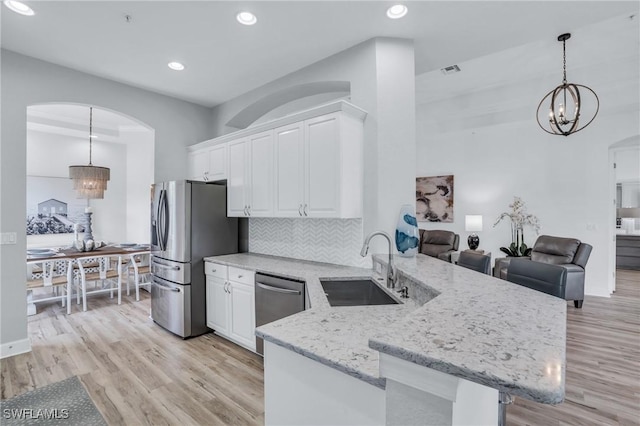 kitchen featuring kitchen peninsula, white cabinets, hanging light fixtures, and appliances with stainless steel finishes