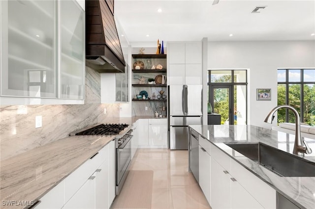 kitchen featuring modern cabinets, custom range hood, open shelves, a sink, and appliances with stainless steel finishes