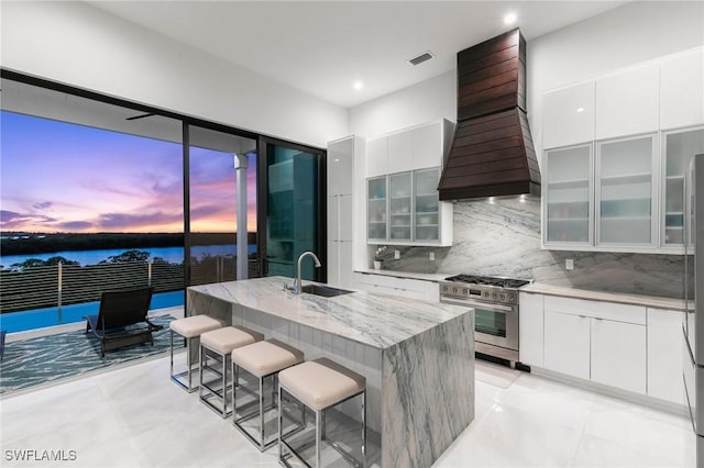 kitchen with a breakfast bar, a sink, custom range hood, high end stainless steel range oven, and modern cabinets