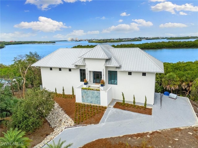 view of front of house with metal roof, a water view, stucco siding, and a standing seam roof