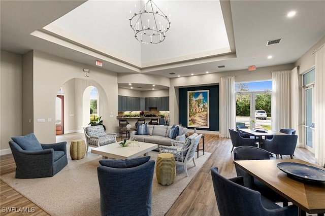 living area featuring light wood-style floors, a raised ceiling, a notable chandelier, and visible vents