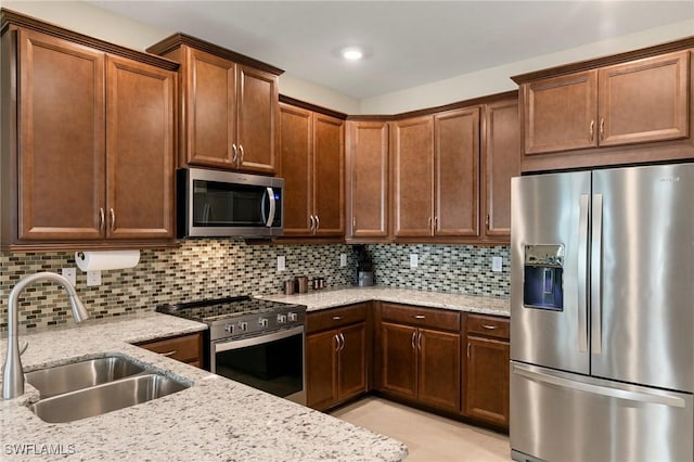 kitchen with light stone countertops, appliances with stainless steel finishes, decorative backsplash, and sink