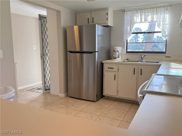 kitchen with sink, light tile patterned floors, cream cabinets, range, and stainless steel refrigerator