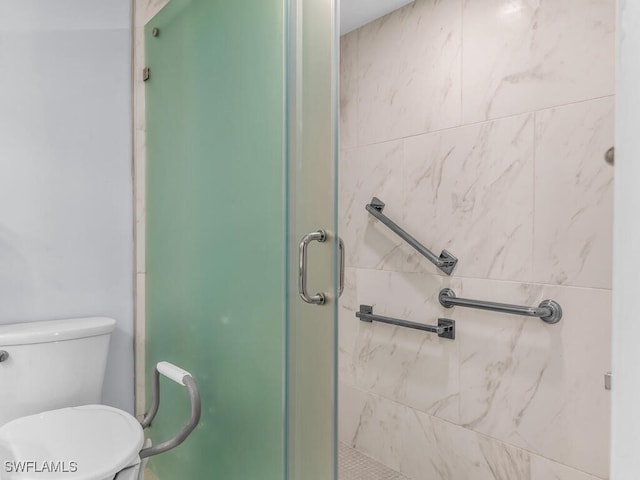 bathroom featuring a shower with door and toilet