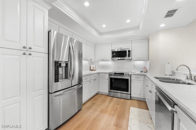 kitchen featuring a raised ceiling, sink, light wood-type flooring, appliances with stainless steel finishes, and white cabinetry