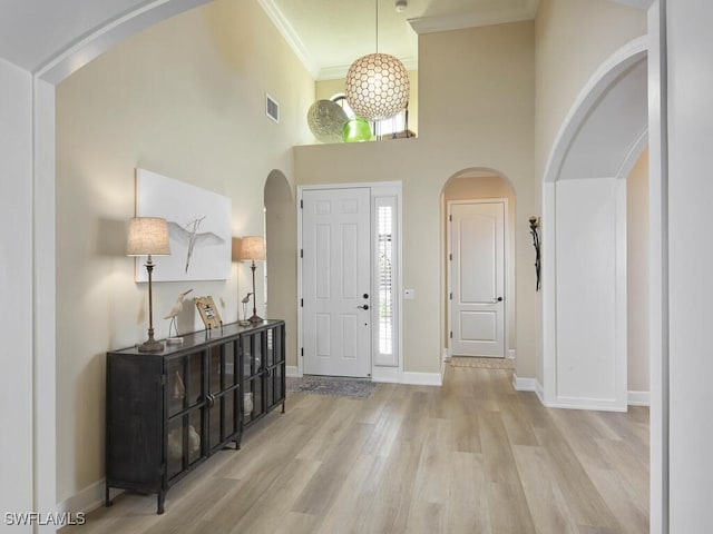 foyer featuring light wood-type flooring, a towering ceiling, and crown molding